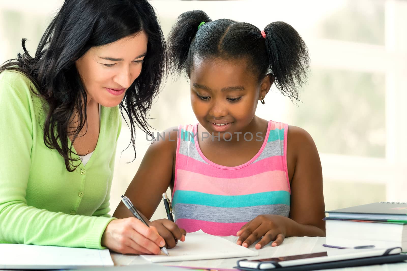 Caucasian teacher helping little african student at desk with sc by karelnoppe