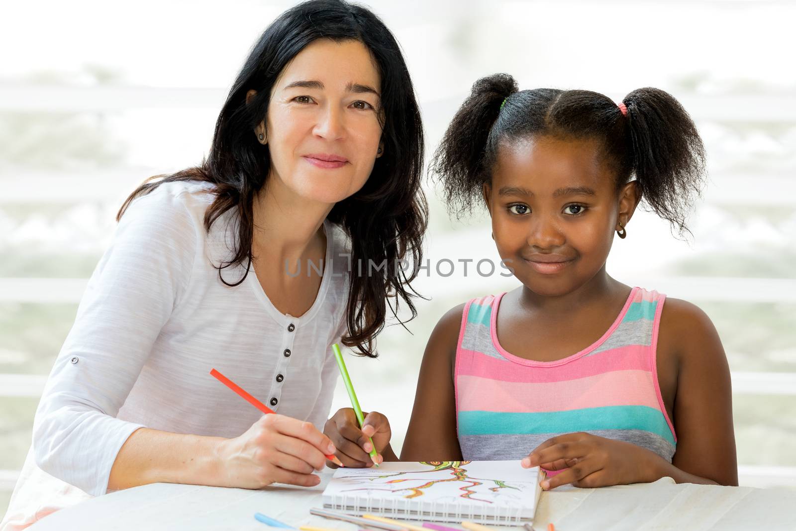 Close up portrait of little african girl and caucasian teacher at home. Kid having private art drawing after school lesson.