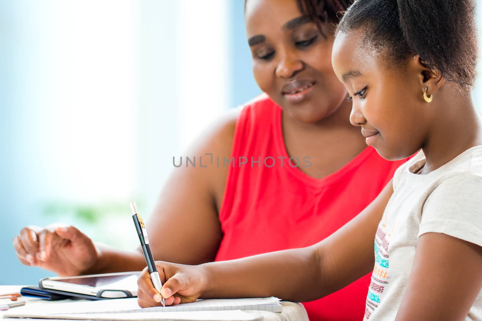 Close up portrait of little african girl doing home work. Teacher giving private after school lessons with digital tablet at home.