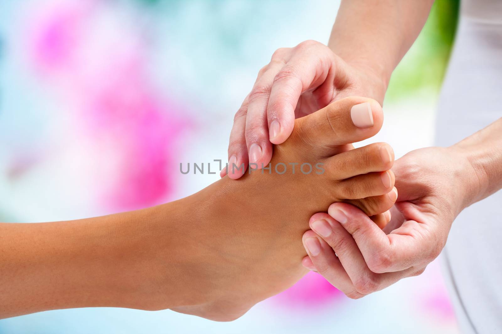 Extreme close up of physiotherapist doing reflexology massage on female foot. Colorful background.