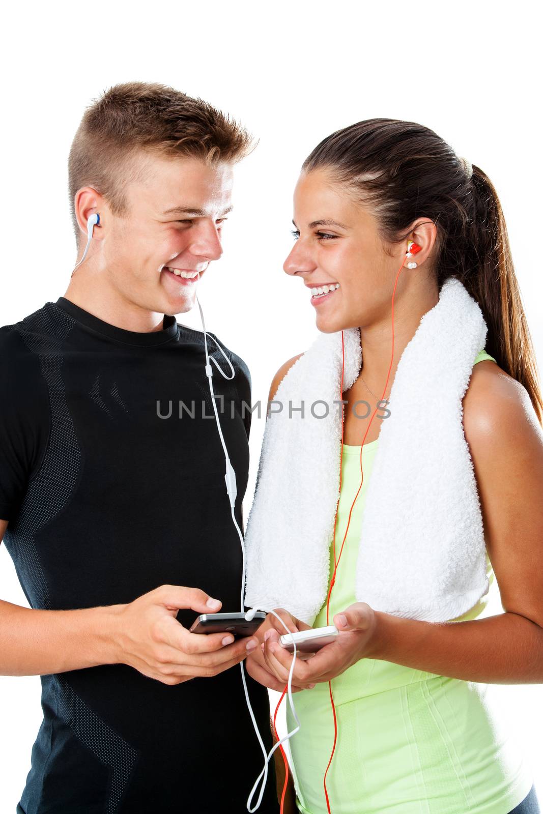 Close up portrait of handsome teen fitness couple standing with smart phones.Couple in sportswear with earphones isolated on white background.