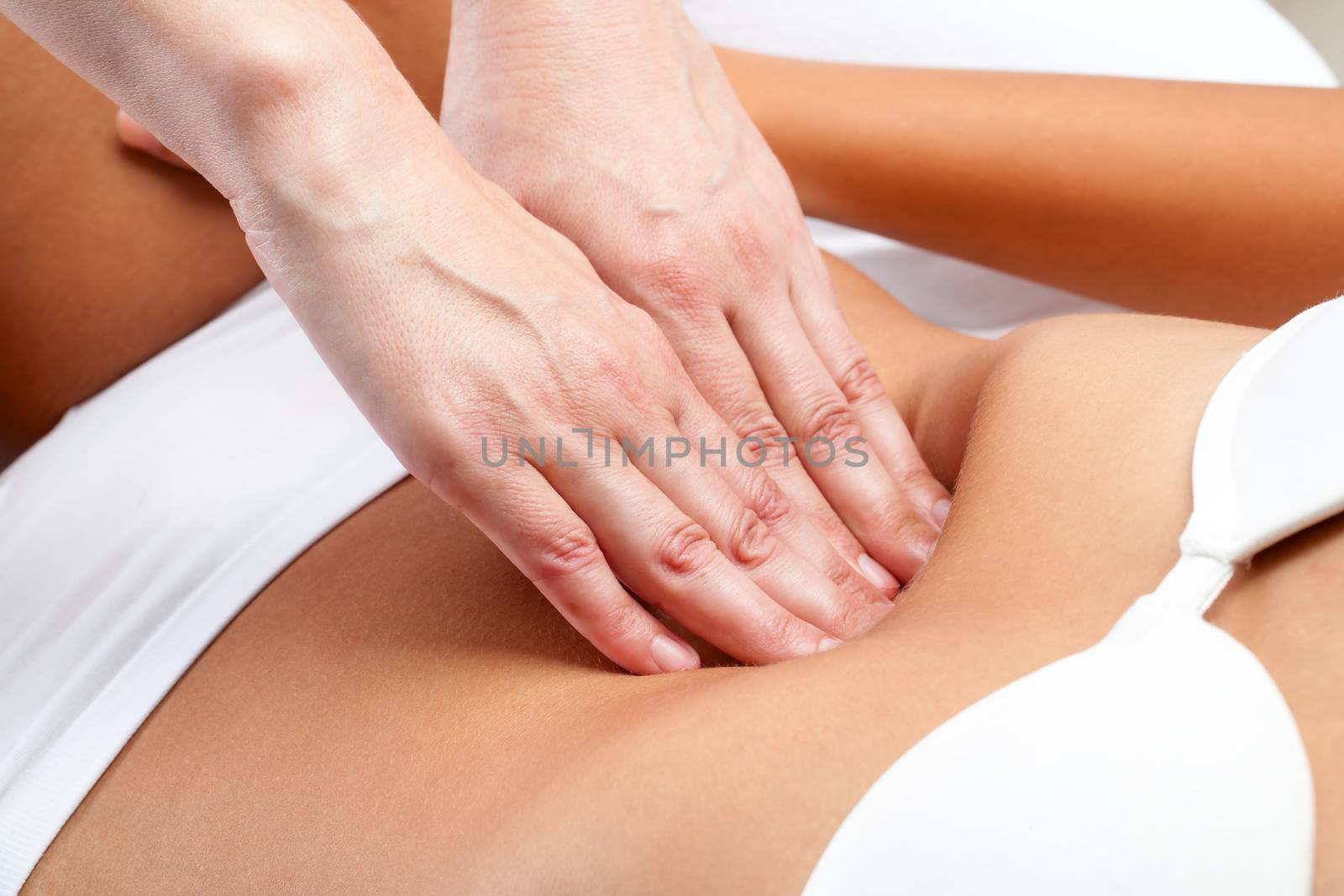 Macro close up of therapist hands doing visceral massage on female abdomen.