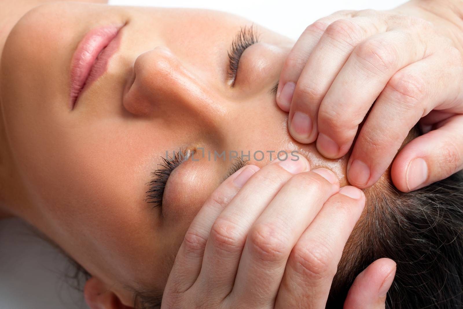 Macro close up face shot of young woman receiving massage. Therapist hand doing manipulative treatment on forehead.