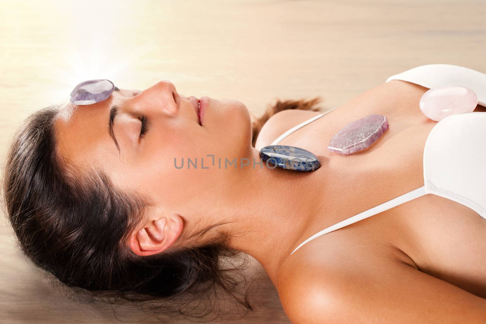 Close up of attractive young woman meditating with eyes closed. Precious gemstones on top of forehead and chest.