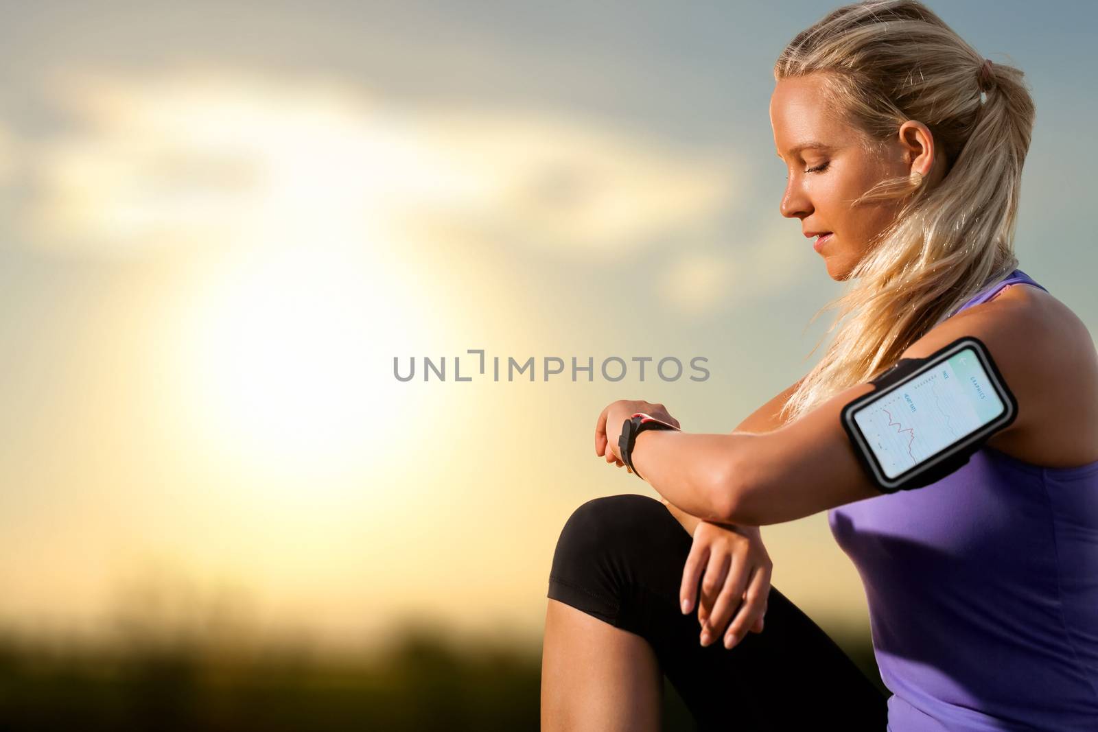 Portrait of young athlete checking workout on smart watch at sunset.Woman wearing armband with smart watch and graphic showing workout results.