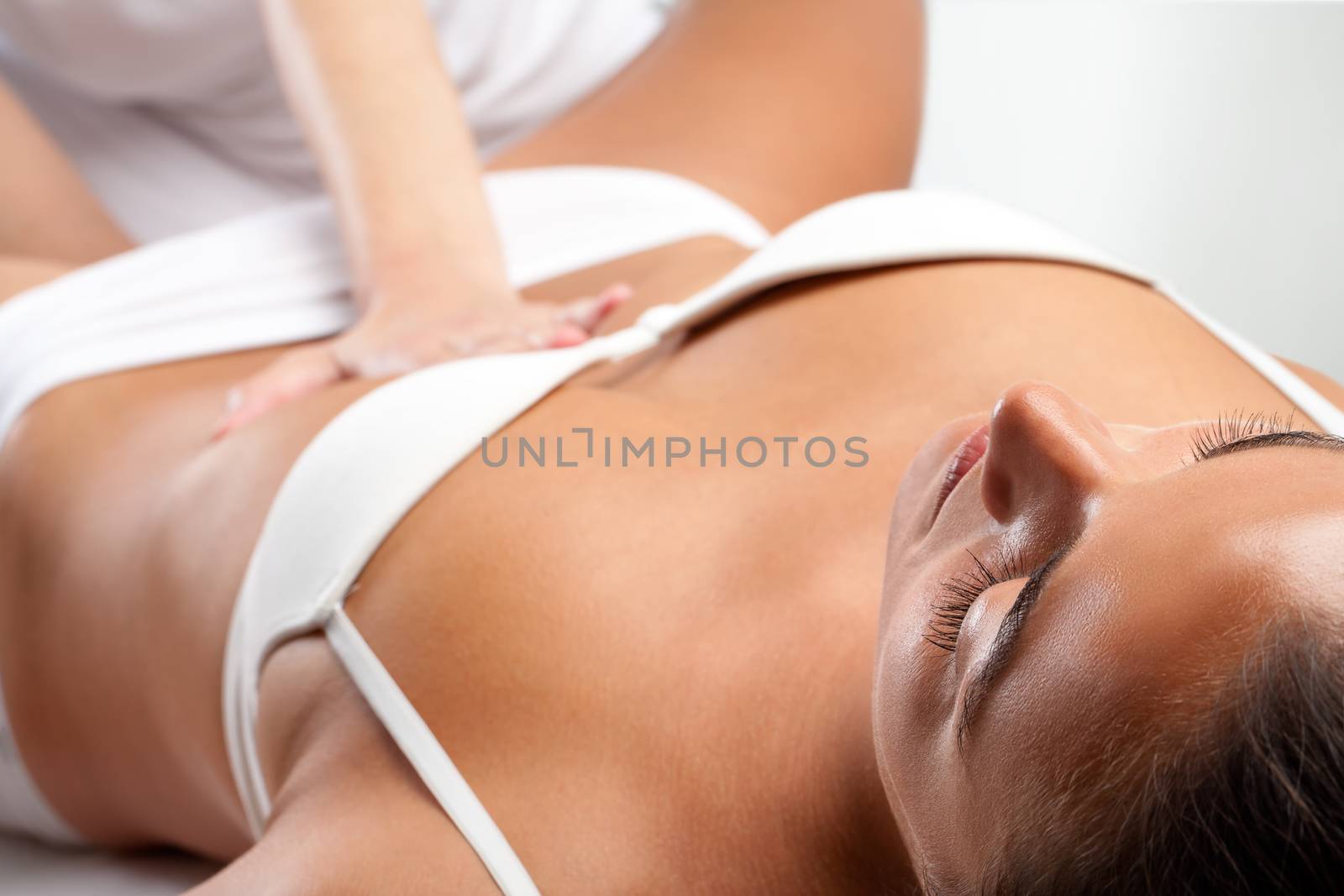 Close up of young woman receiving osteopathic visceral massage with therapist hand pressing on stomach.