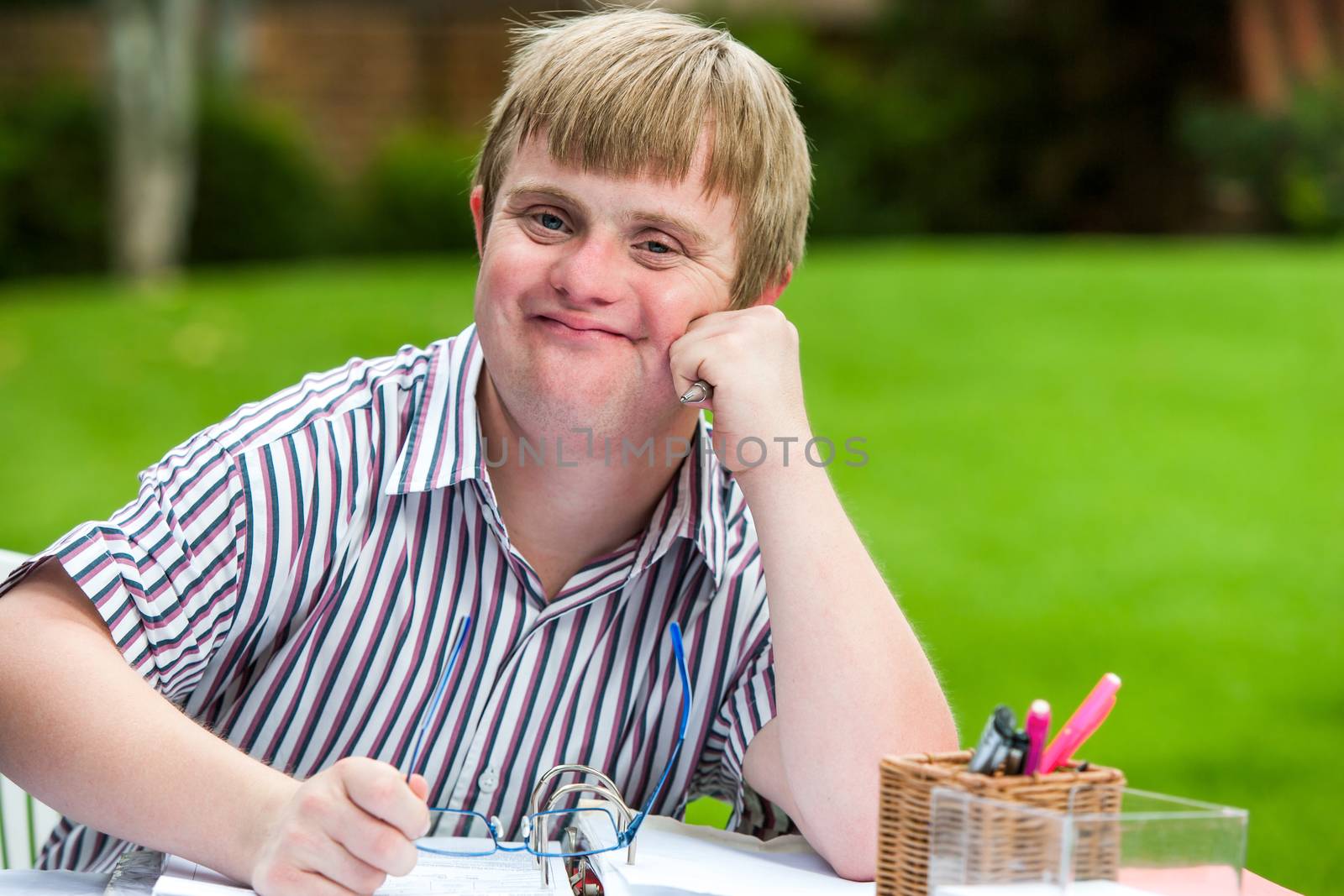 Boy with down syndrome at desk holding glasses. by karelnoppe