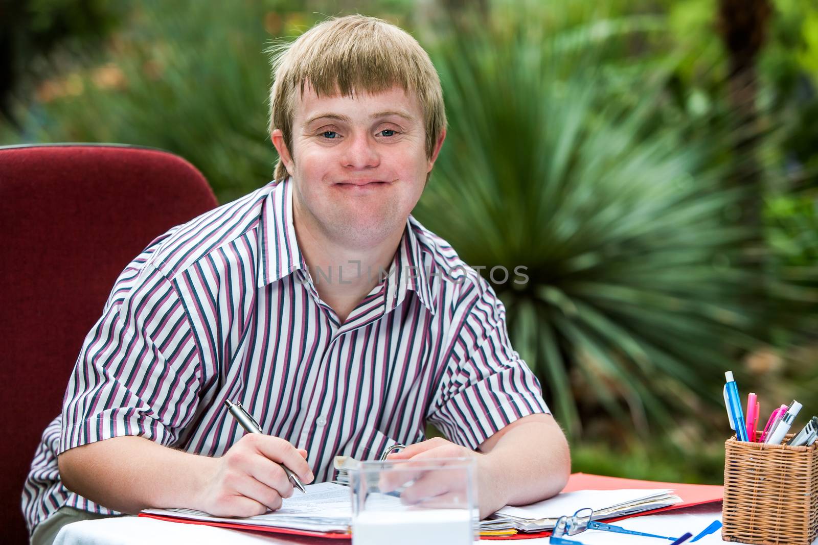 Boy with down syndrome at desk outdoors. by karelnoppe