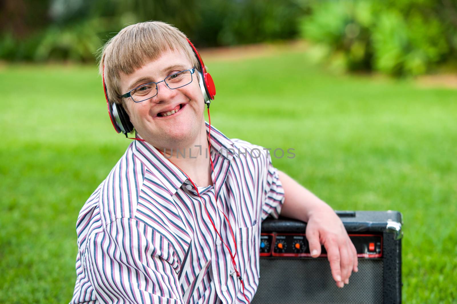 Close up portrait of young man with down syndrome wearing headphones outdoors.

