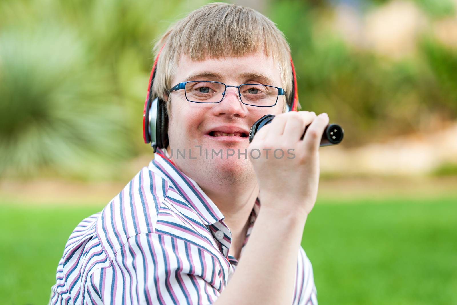 Close up portrait of young handicapped man singing with microphone outdoors.
