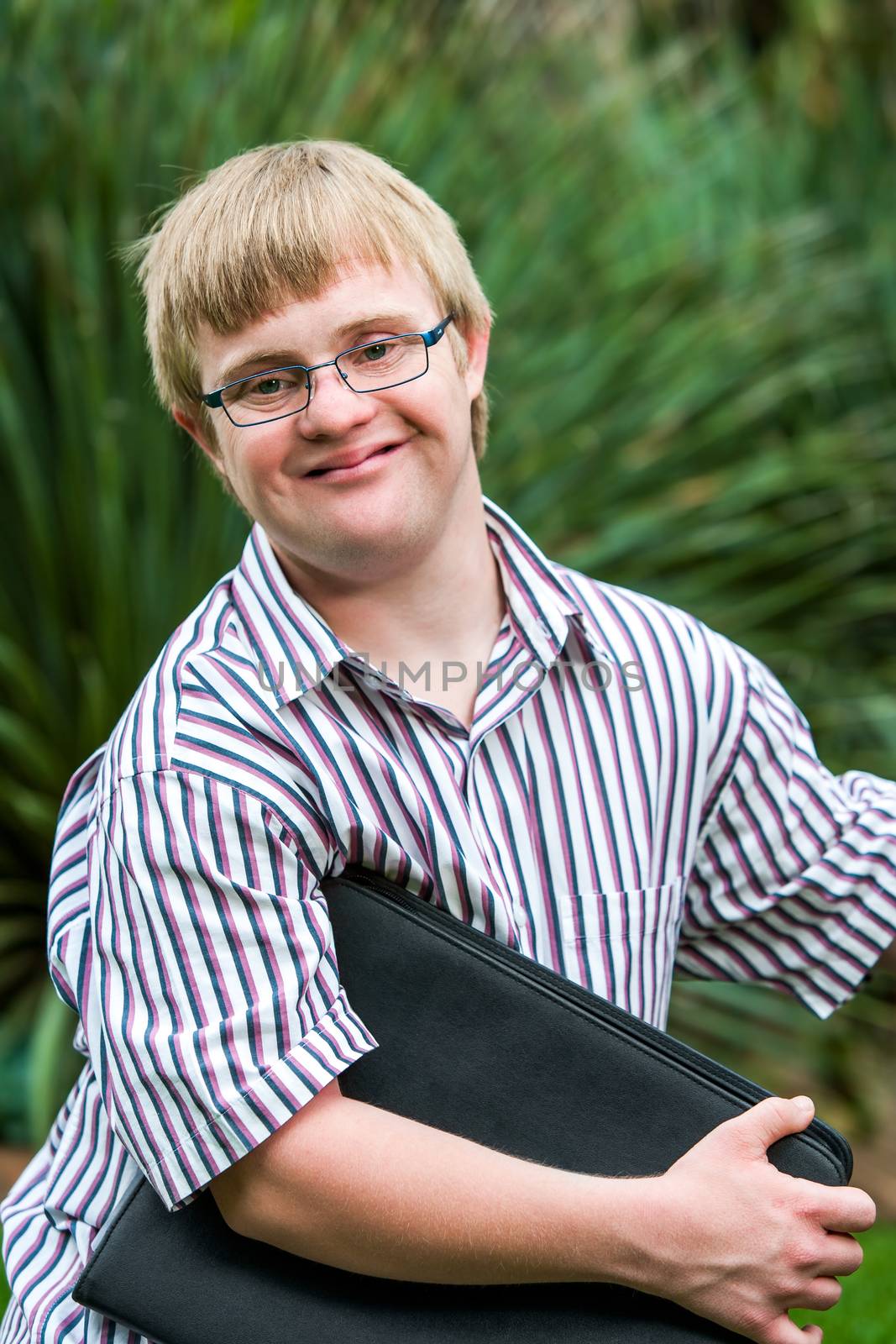 Young student with down syndrome holding files outdoors. by karelnoppe