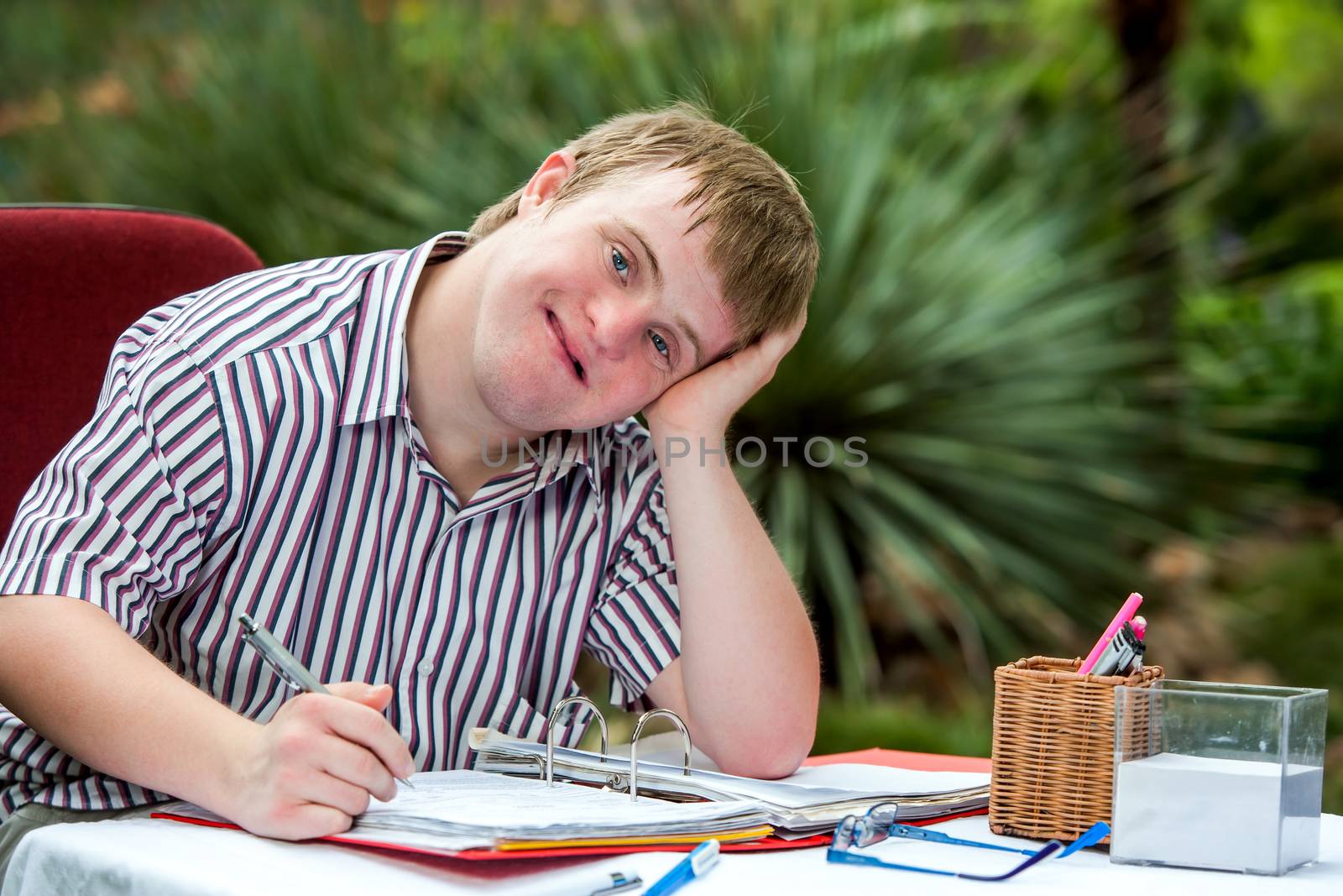 Close up portrait of Handicapped student resting on hand at desk in garden.