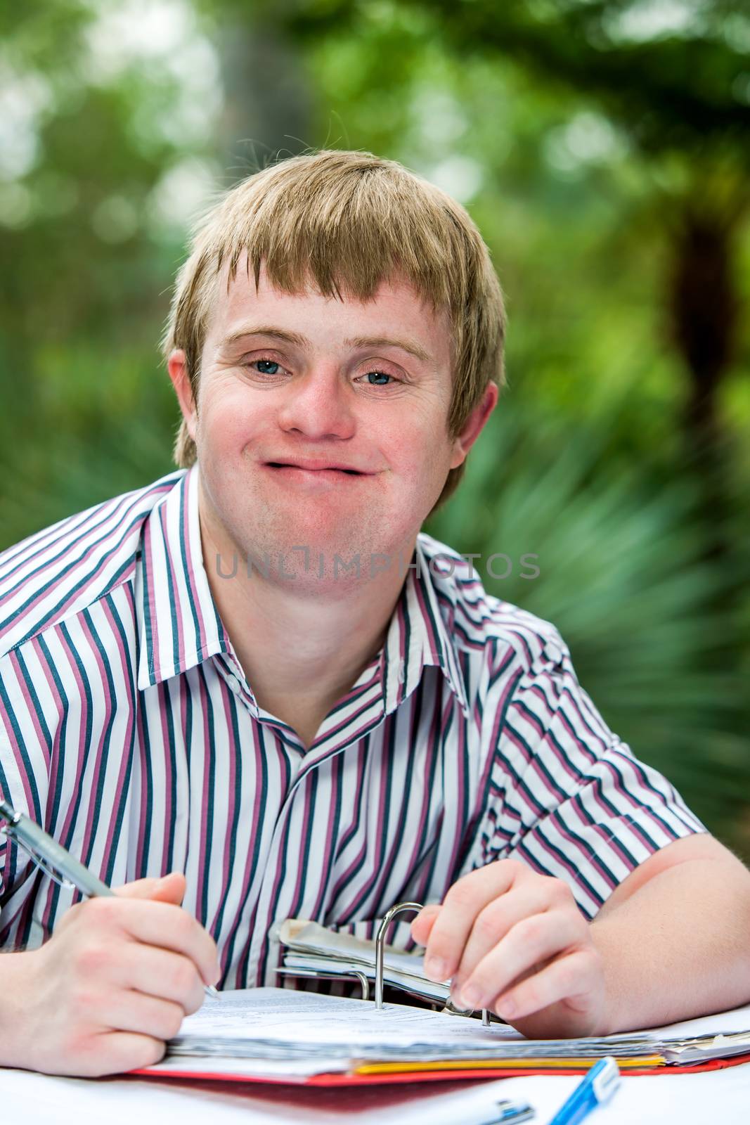 Close up portrait of student holding pen with file on desk.Outdoors in green garden.