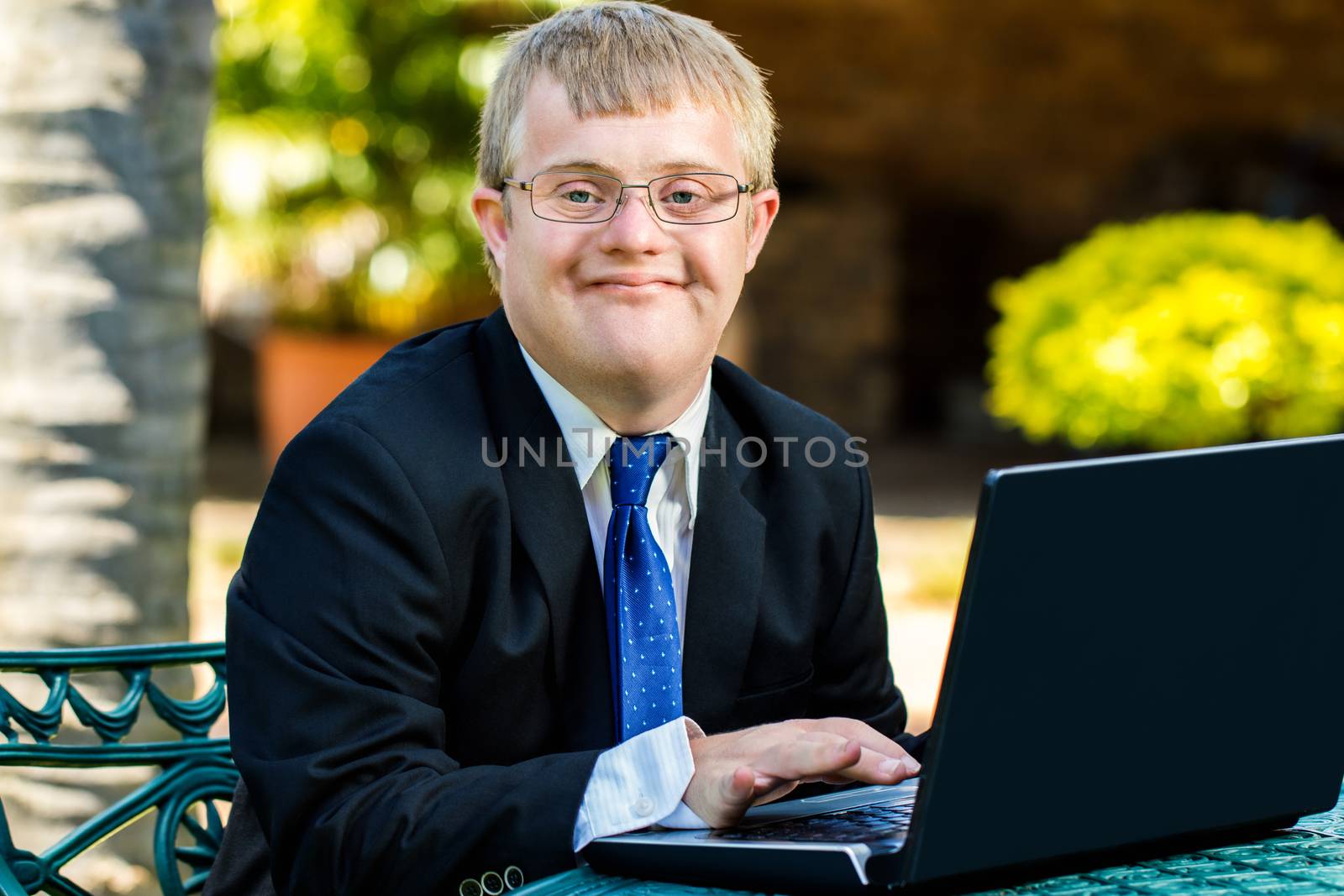 Close up portrait of young businessman with down syndrome doing accounting on laptop outdoors.