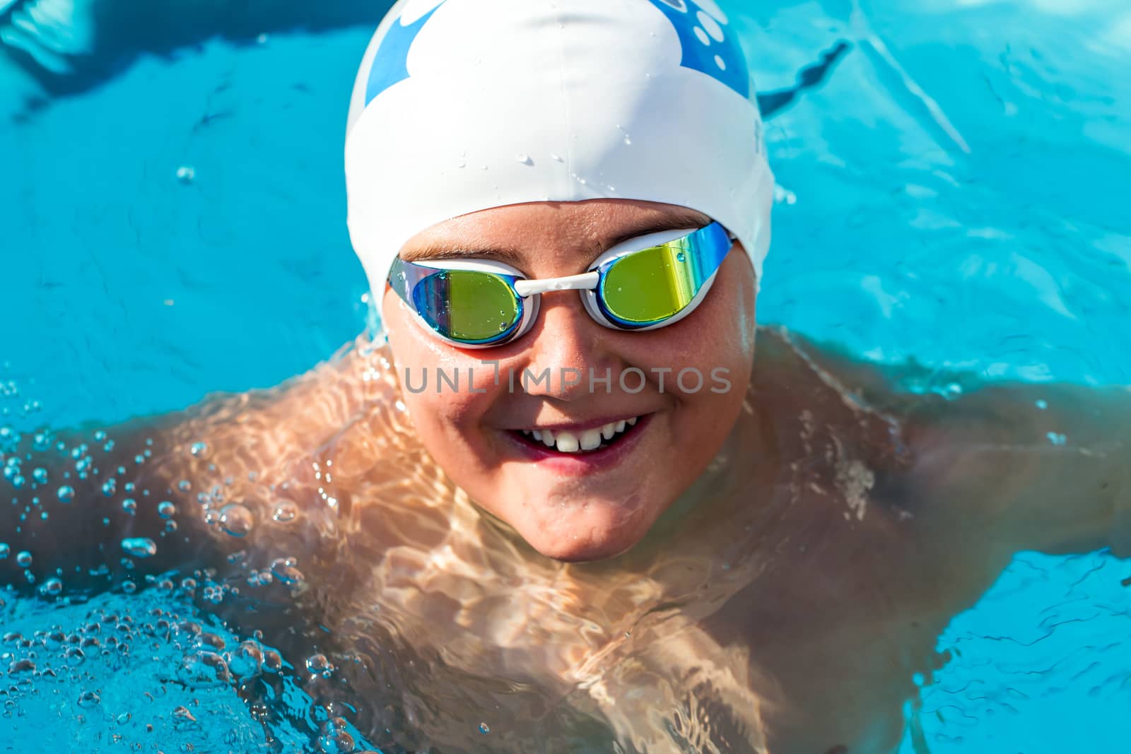 Close up portrait of teenager with swim cap and goggles in swimming pool.