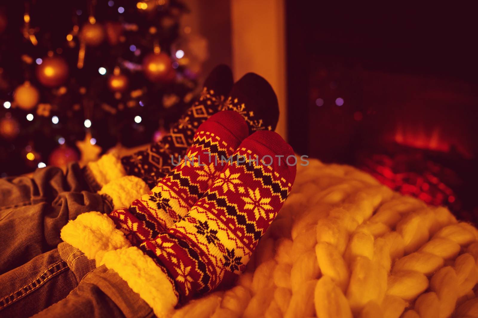 Couple sitting in woolen socks near fireplace in living room decorated for Christmas holidays