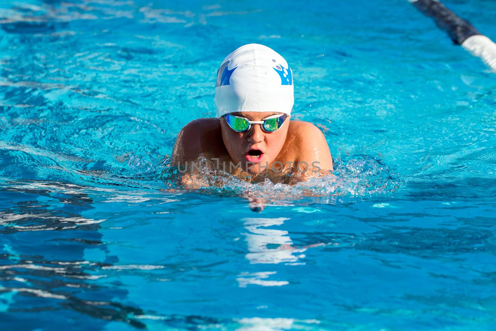Close up action shot of young teen boy practicing breaststroke in swimming pool.