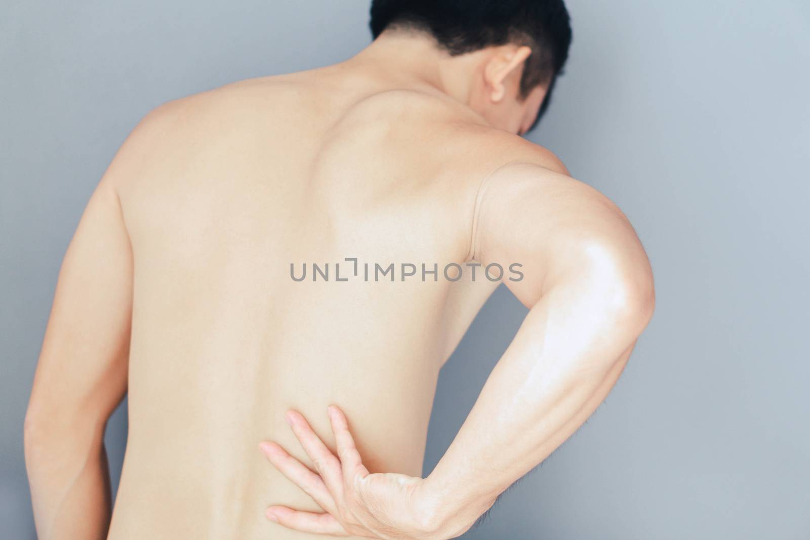 Young man hand holding back with pain on grey background, health care and medical concept