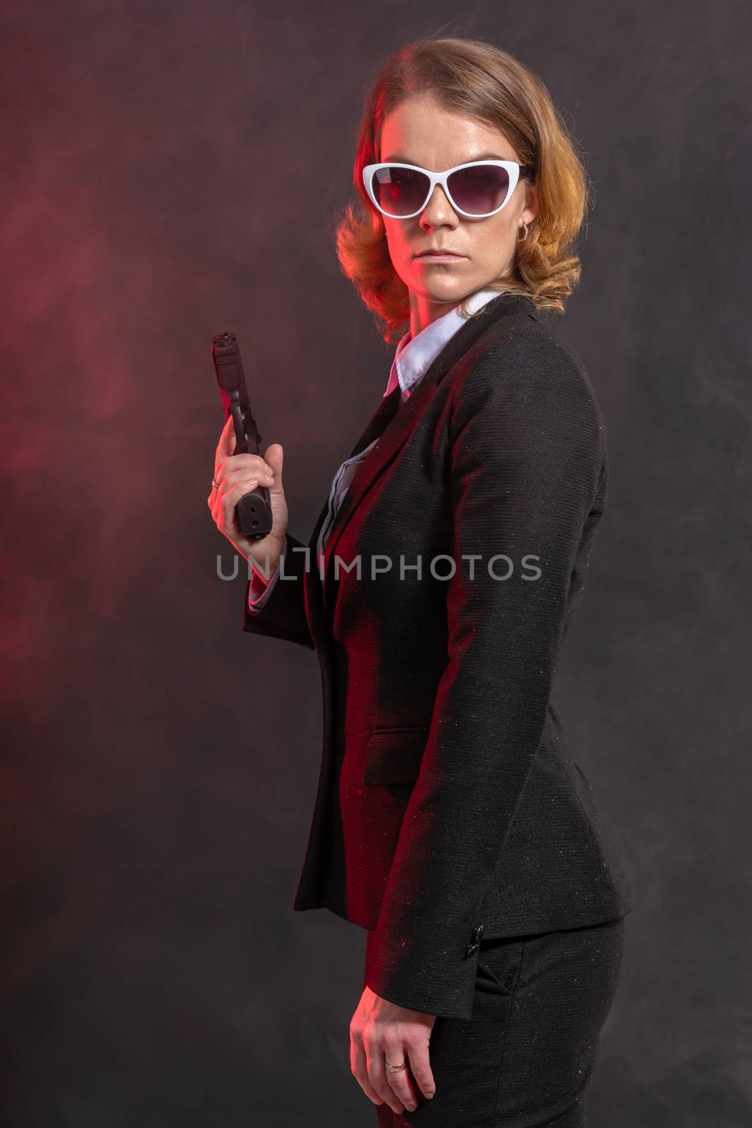 mafian woman with a gun in her hand. portrait on a dark background with red light. white glasses