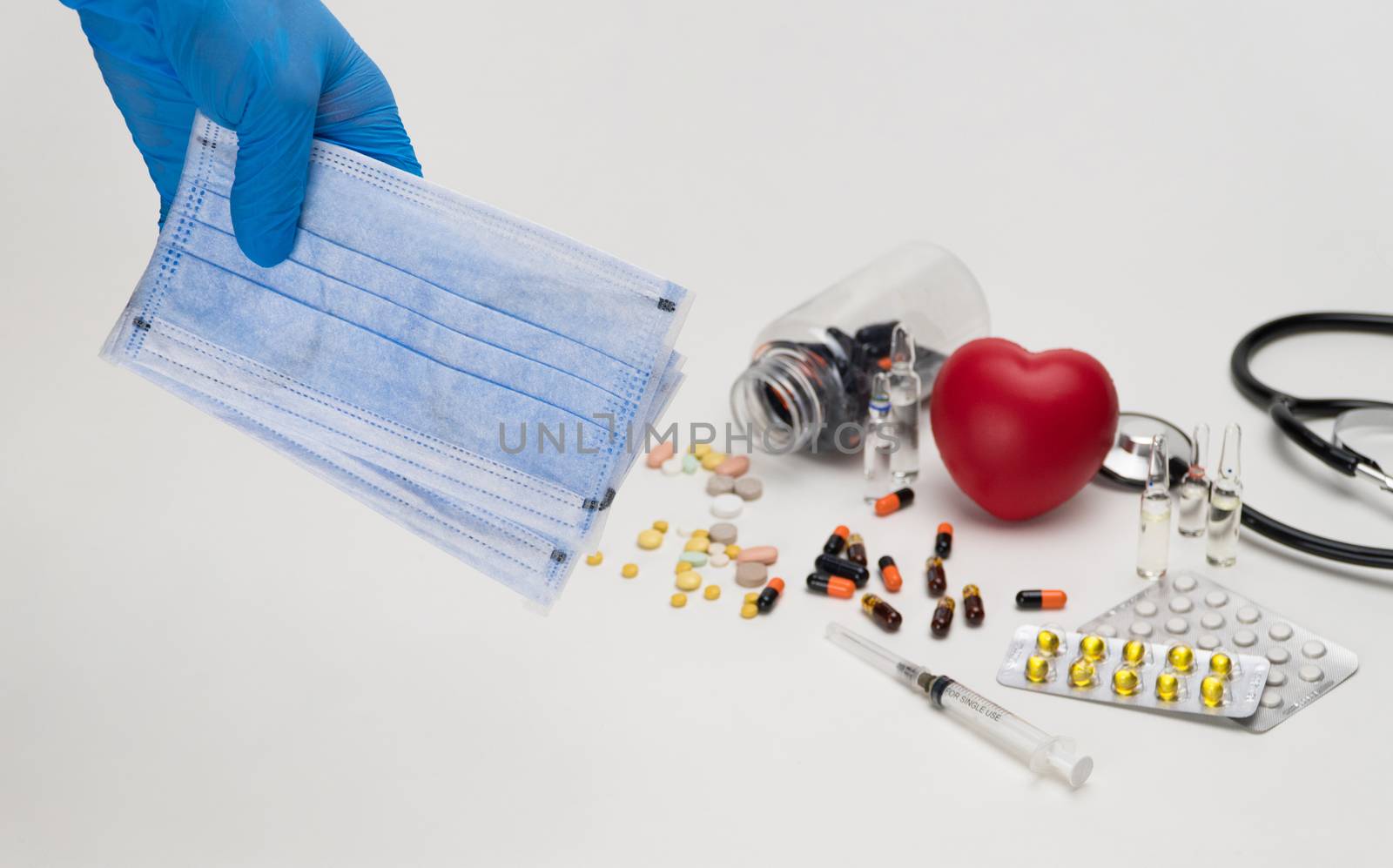 Hand holds a medical mask against a background of a red toy heart and pills. Coronavirus Protection Concept