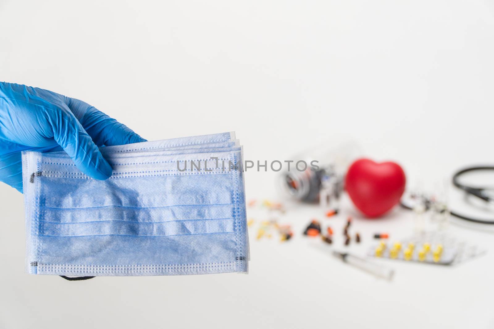 Hand holding a medical mask against the background of a stethoscope and pills. Coronavirus Protection Concept
