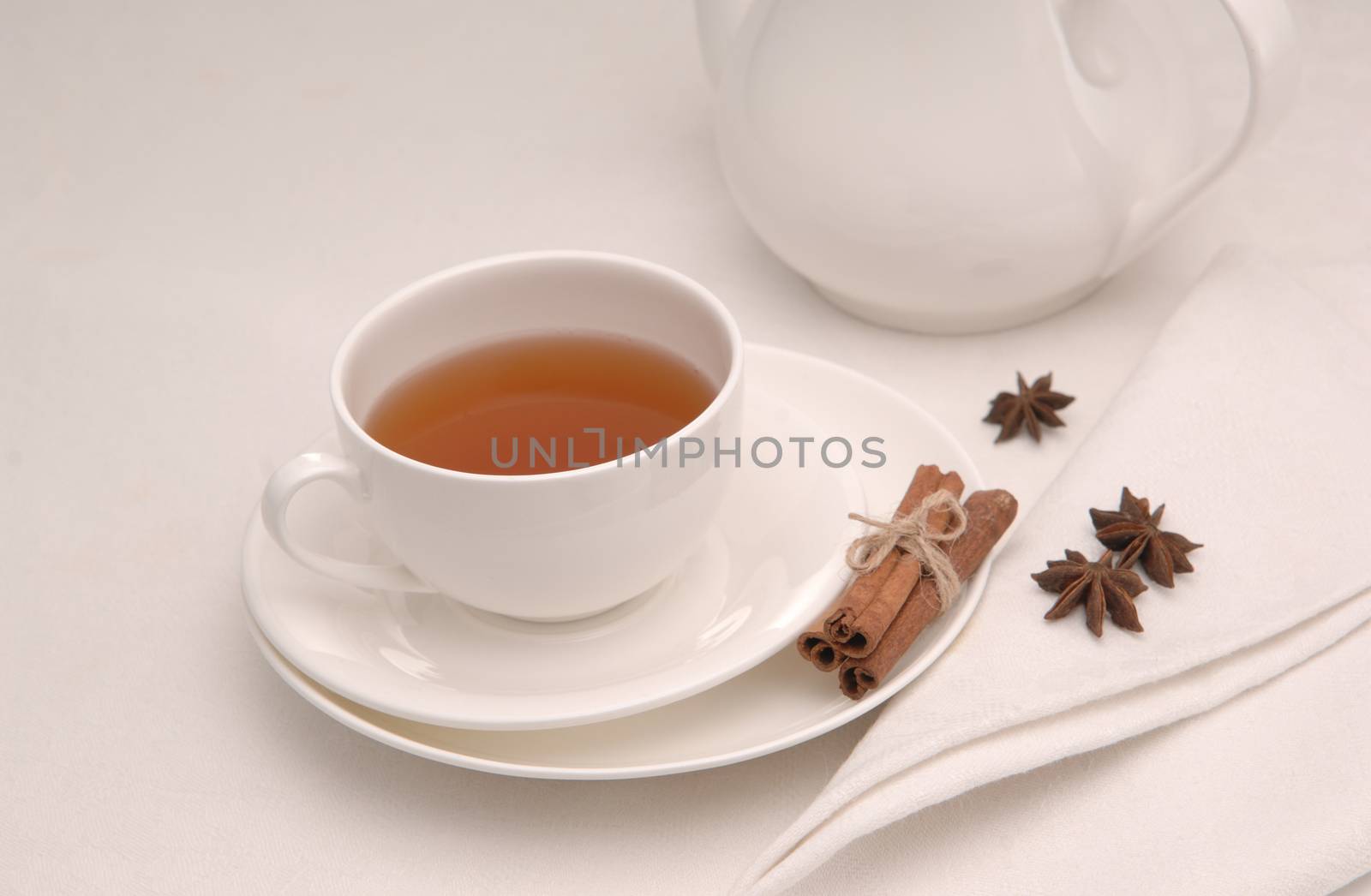 on white napkin tea cup on a saucer and teapot and spices