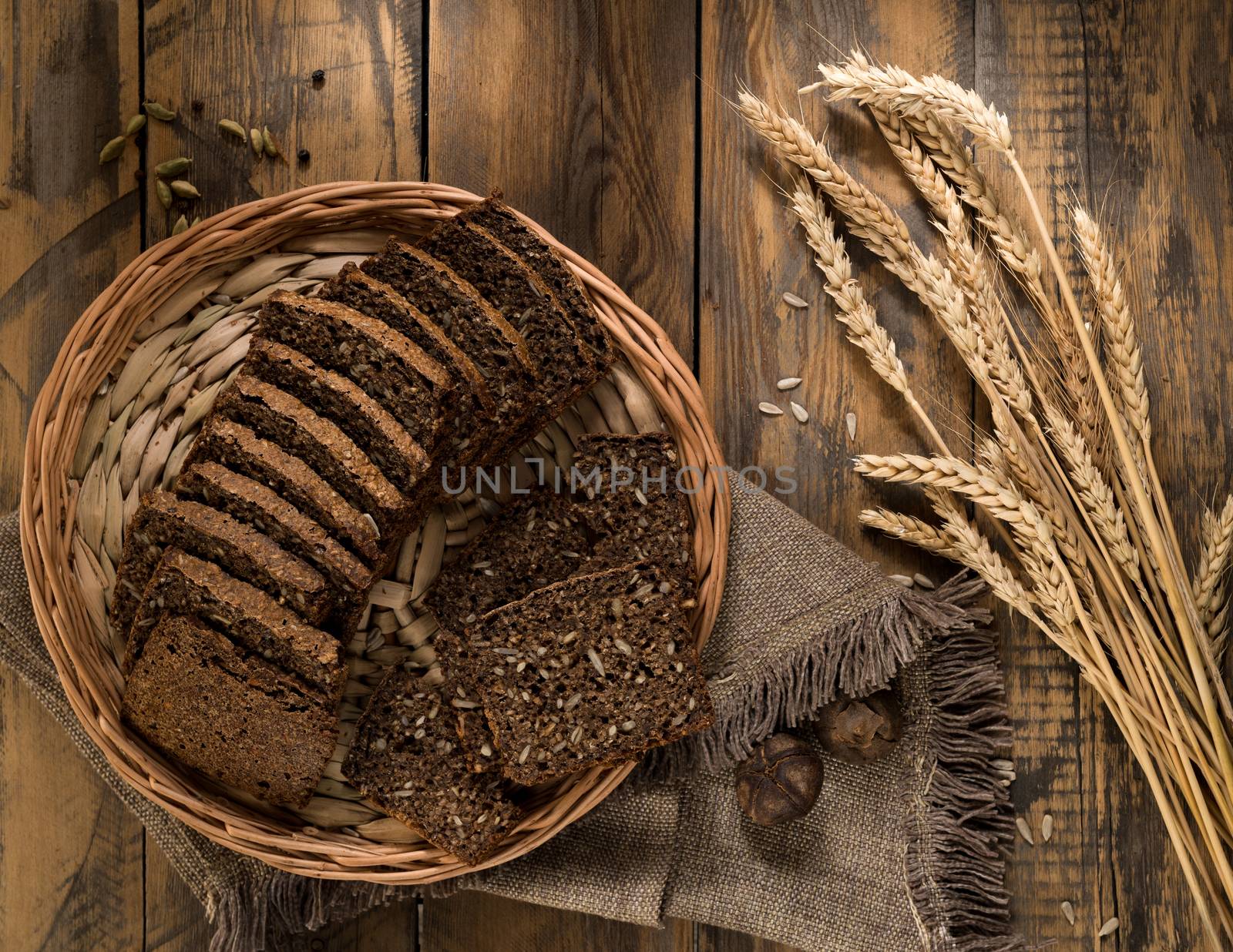 Sliced rye bread in a wicker tray and spikelets on wooden surface