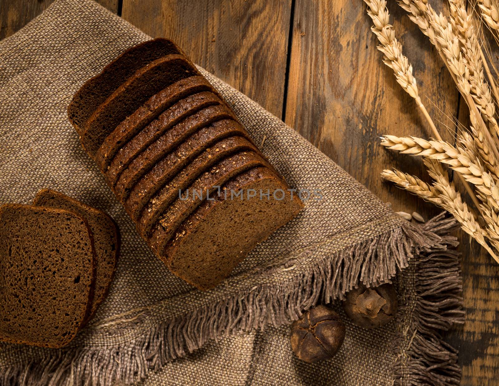 sliced rye bread on a napkin and spikelets on wooden surface, view from above