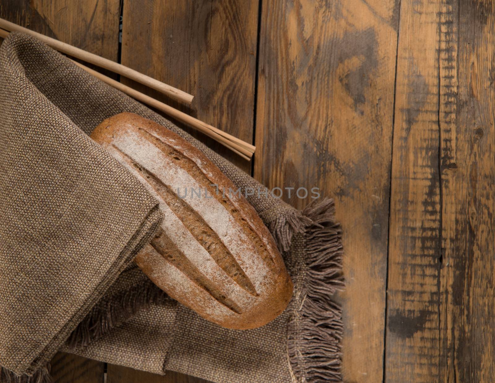 a loaf of bread on a napkin and spikelets on wooden surface, view from above