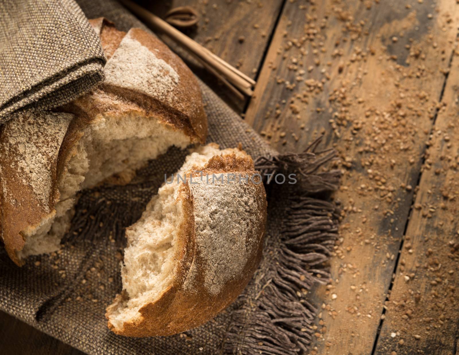 a broken loaf of bread on a cloth napkin and wooden boards with crumbs, top view