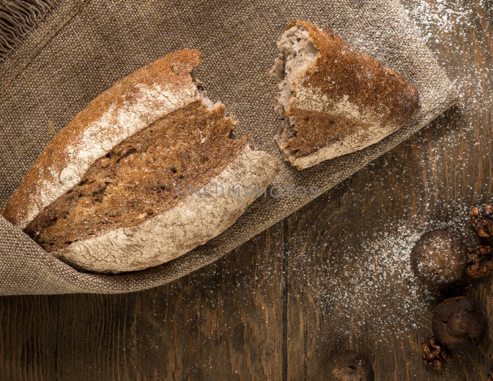 the broken loaf of bread on a cloth napkin and wooden boards, top view