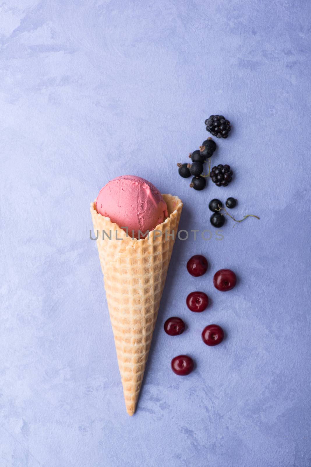 ice cream with berries in a waffle horn on an ornamental purple background, top view