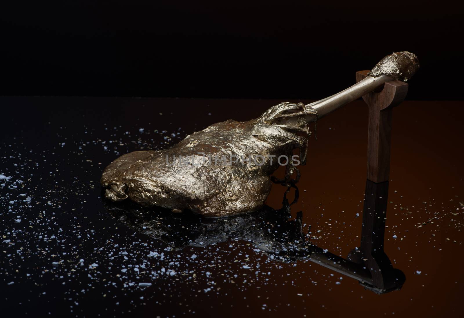 roasted meat with bone in gold leaf on a dark background