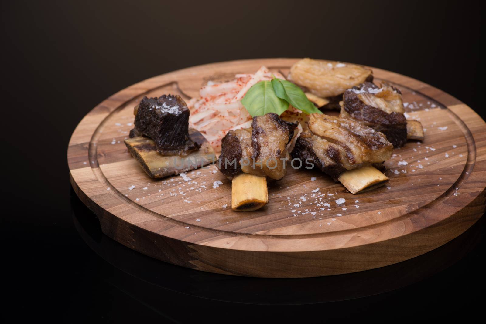 roast meat with bone on a wooden tray, dark background, isolated