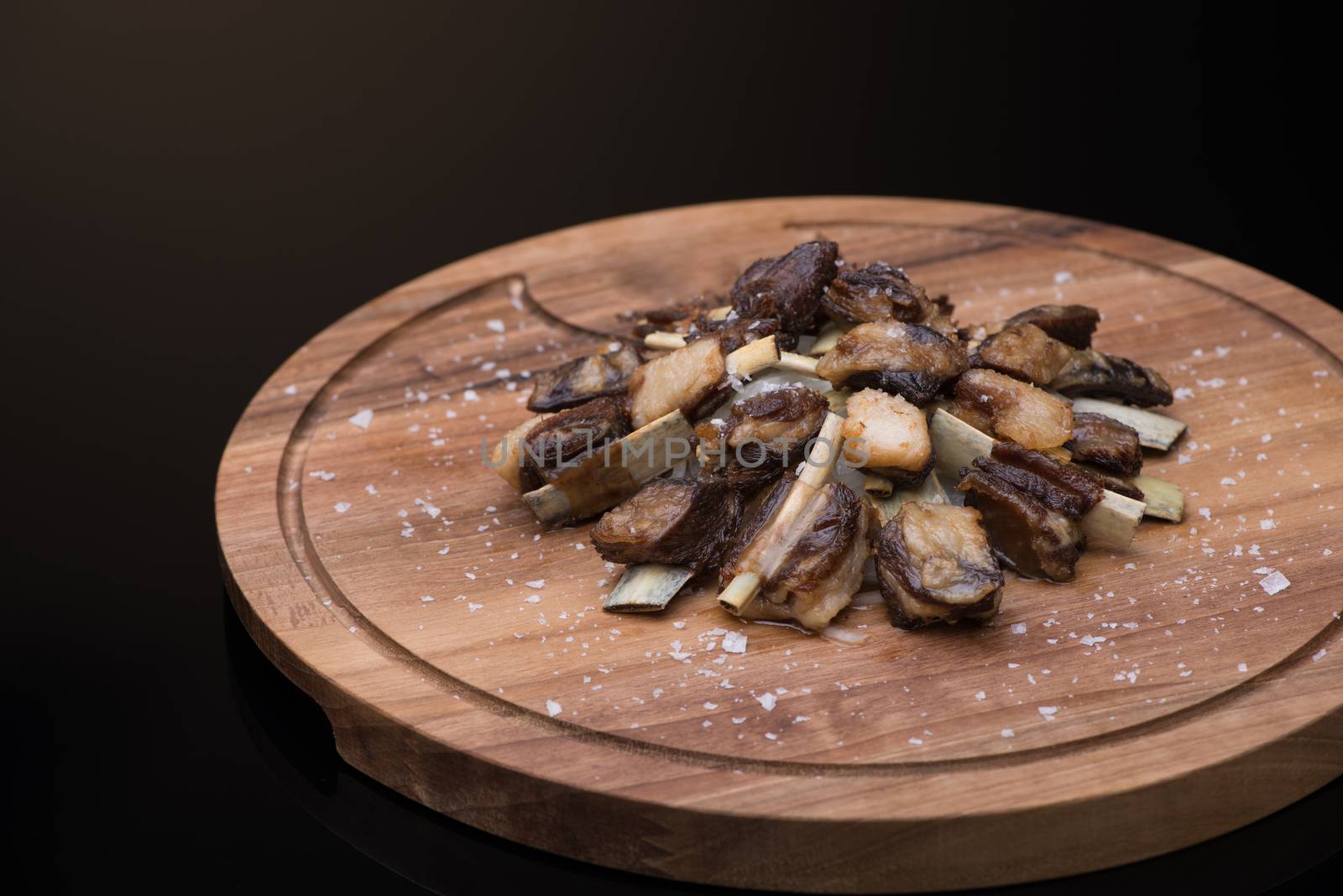 roast meat with bone on a wooden tray, dark background, isolated