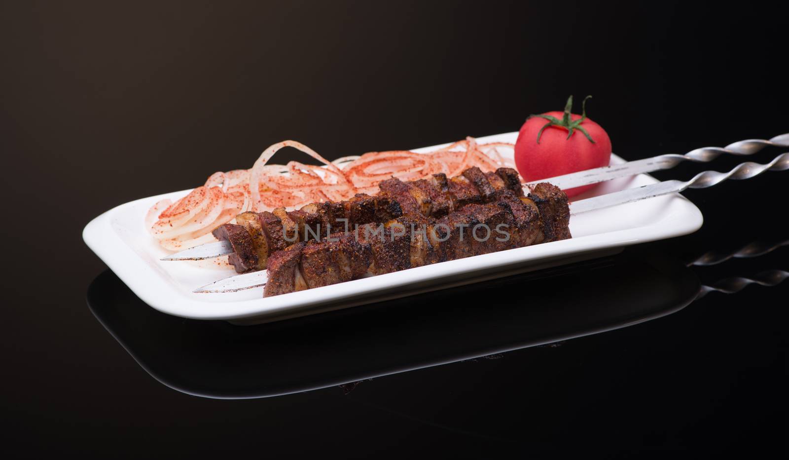 kebab sticks on skewers with onion and tomato on dark background