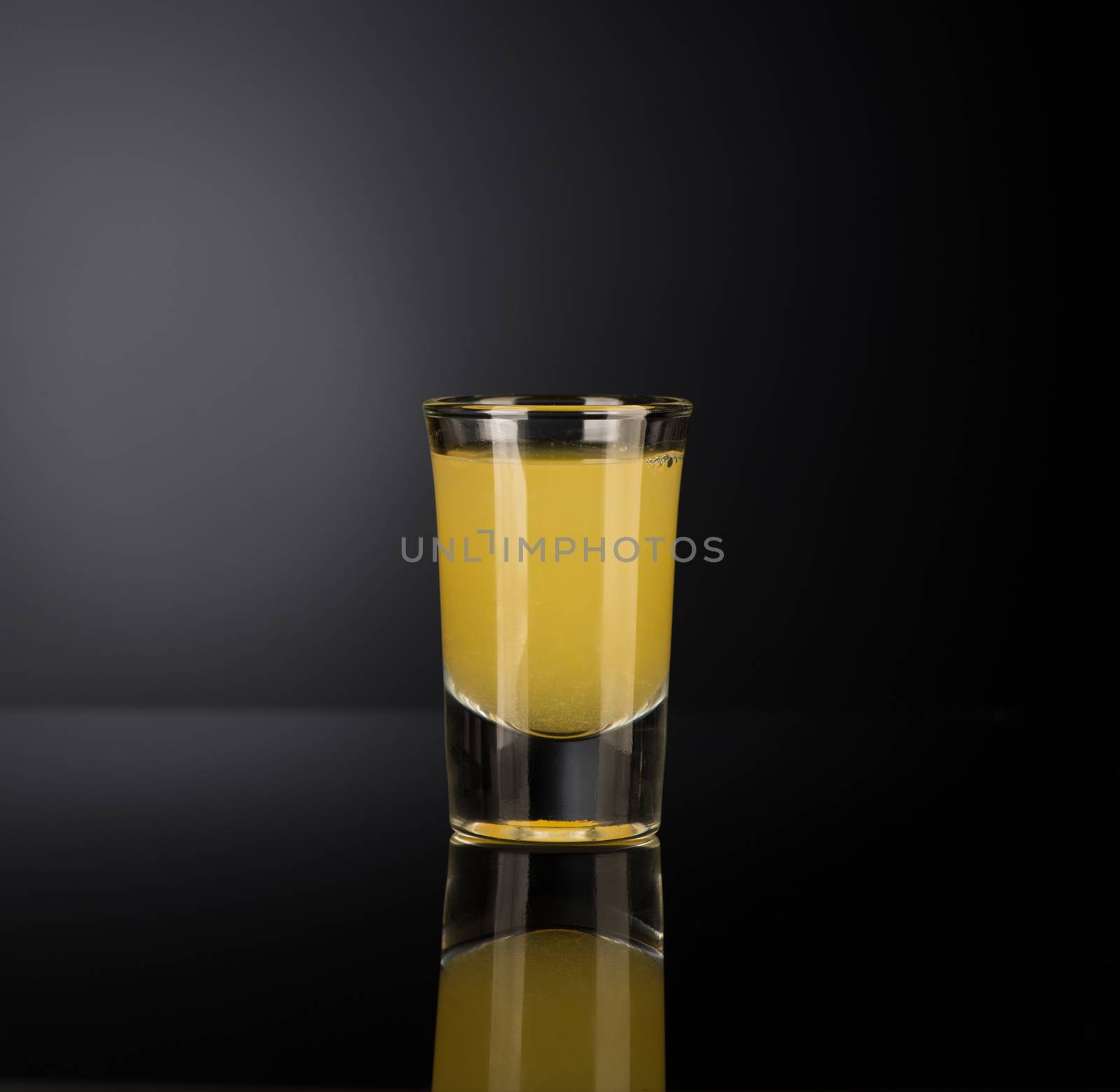 yellow alcoholic liquor in a shot glass isolated on dark background with backlight
