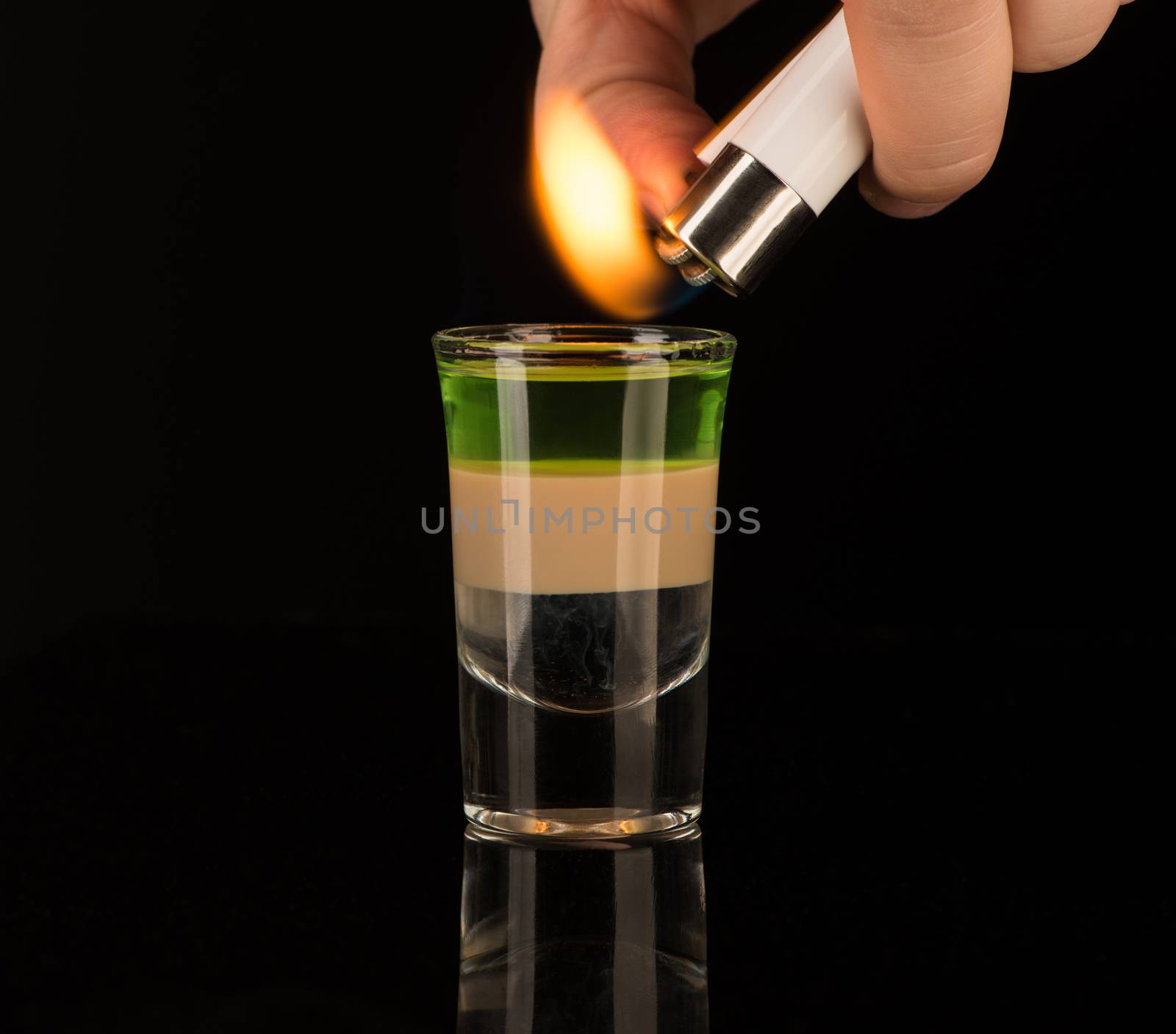 bartender sets fire to a mixed alcoholic cocktail in a shot glass, close-up