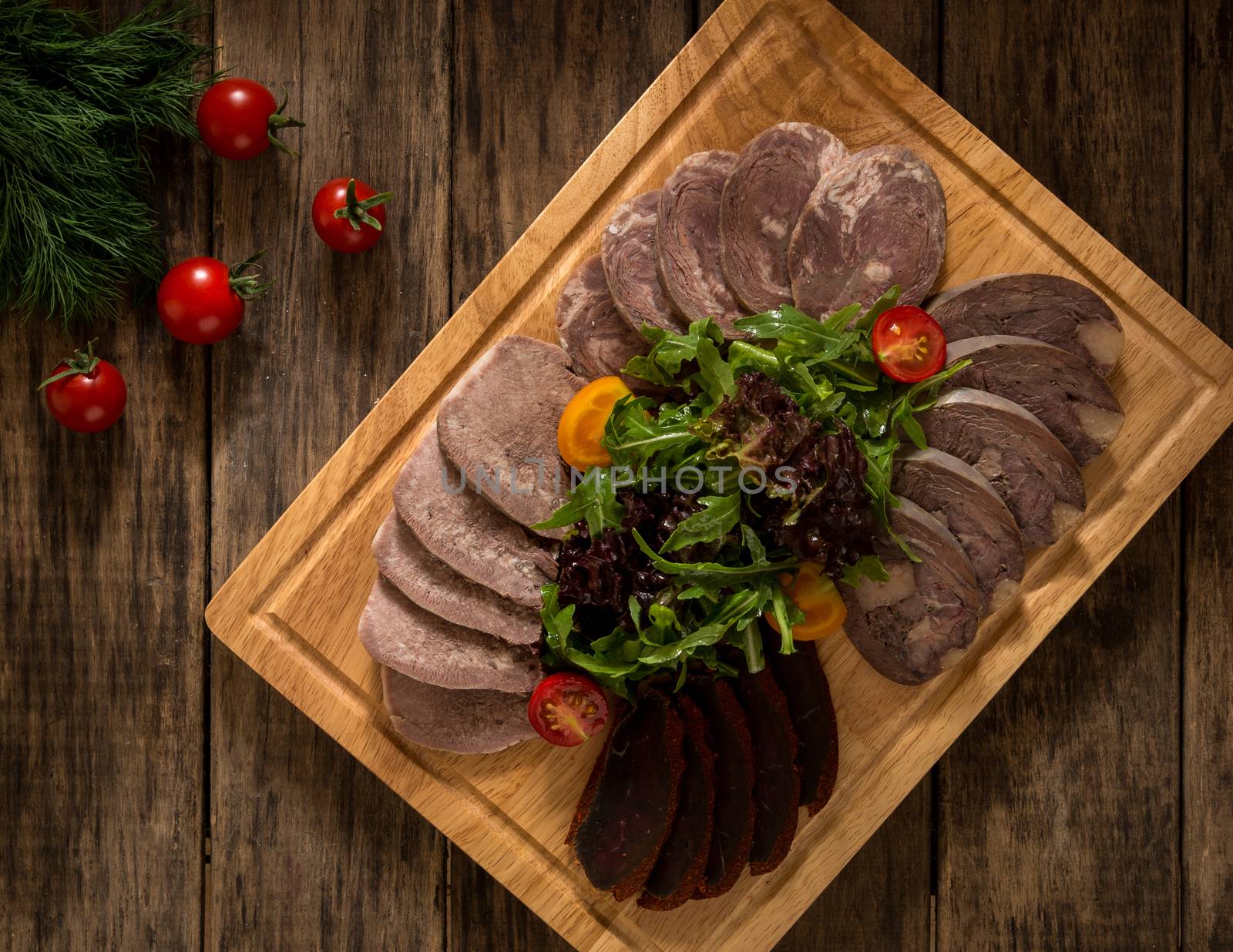 sliced smoked meat on a cutting board decorated with vegetables, top view