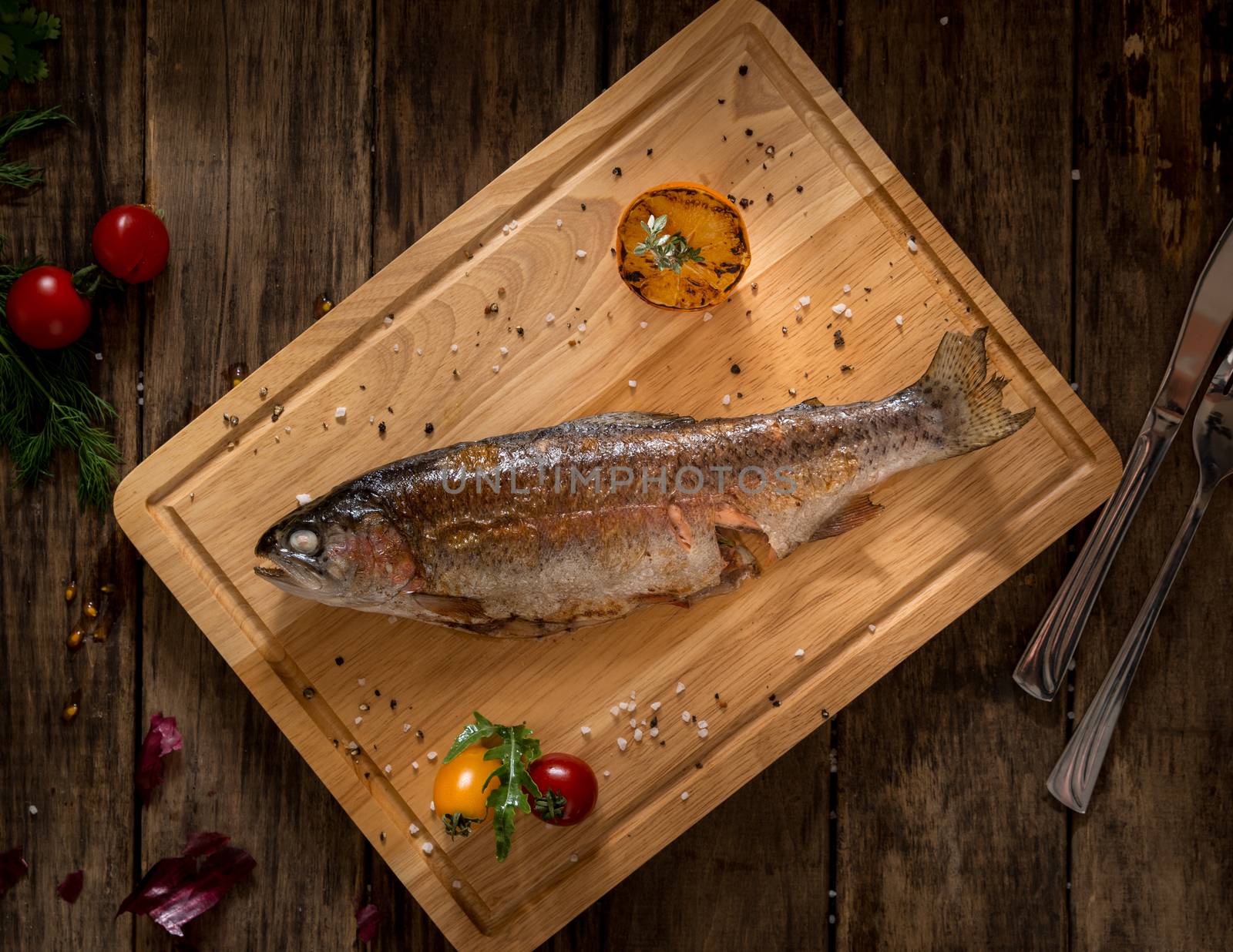 baked fish on a chopping board decorated with tomato and lemon, top view