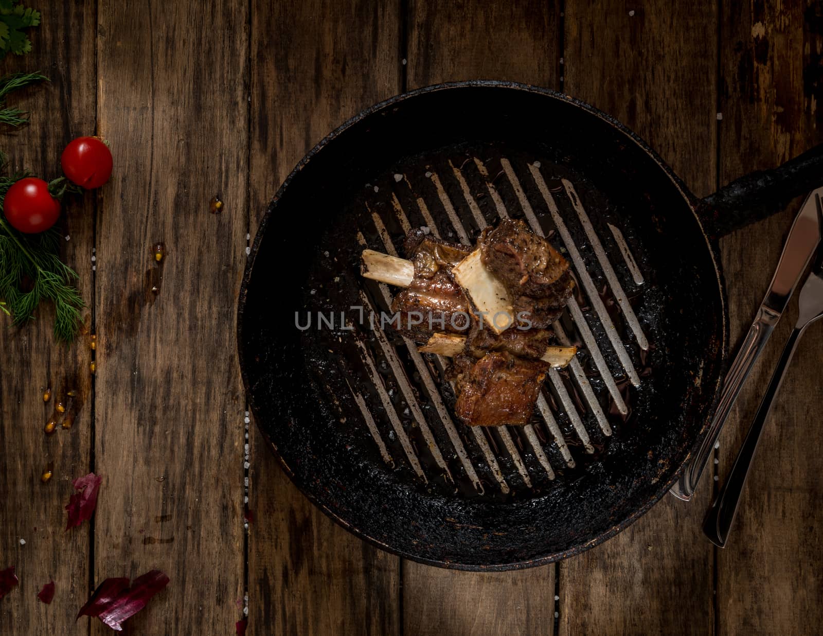 in old pan fried meat with bone on wooden background, top view