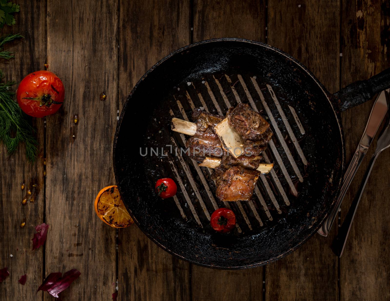 fried meat with bone in the pan on wooden background, top view