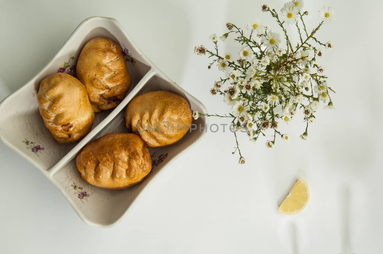 pies and chamomile flowers on a white surface with a shadow from the wine glasses