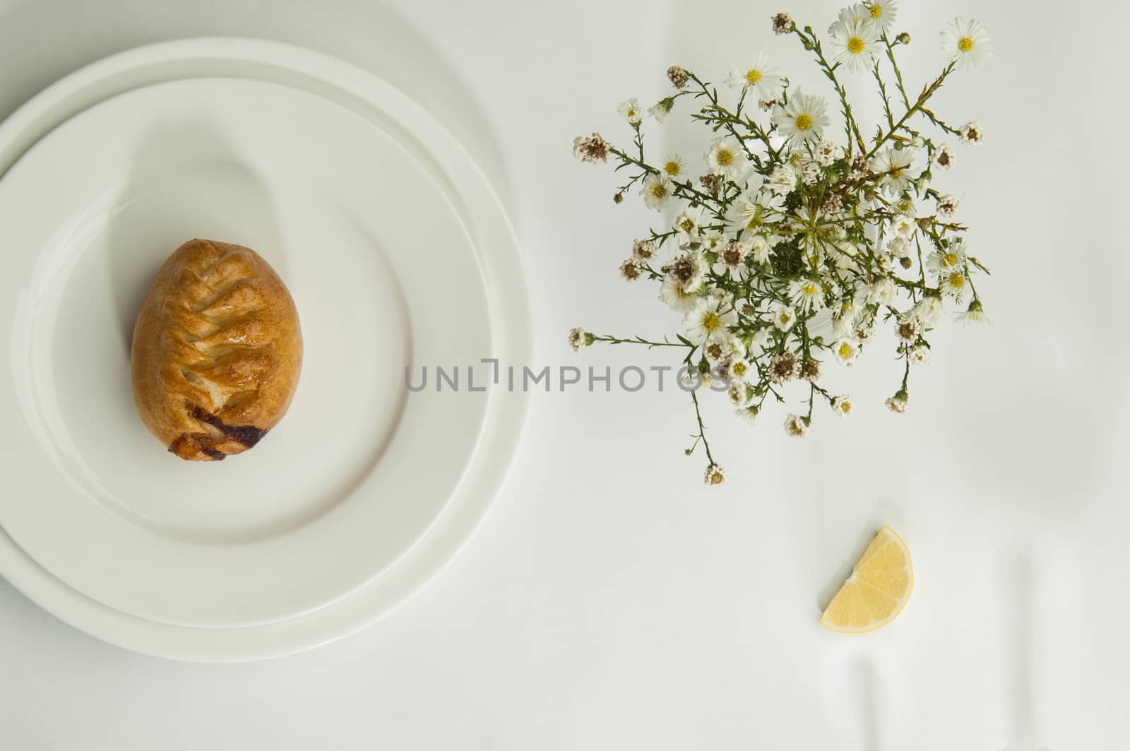 pies and chamomile flowers on a white surface with a shadow from the wine glasses