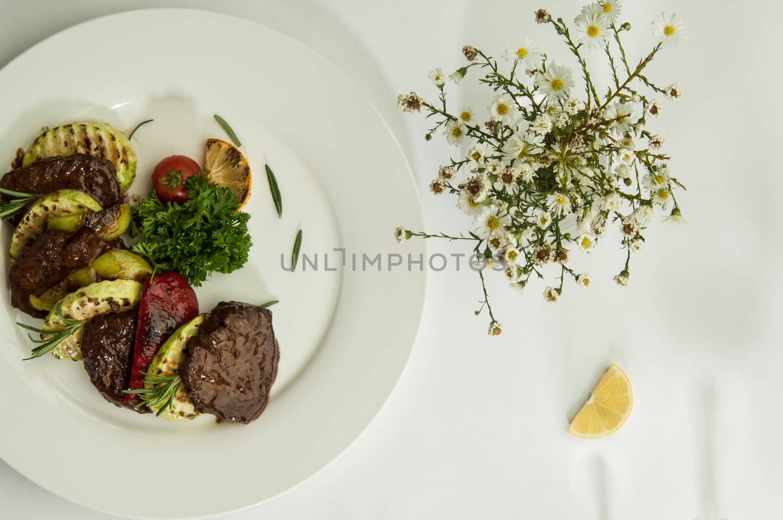 roast meat with lemon slices on a white surface with a shadow from the wine glasses