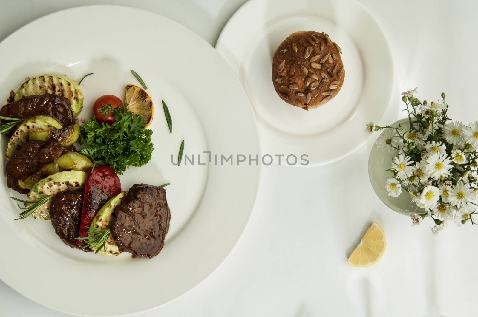 roast meat with lemon slices on a white surface with a shadow from the wine glasses