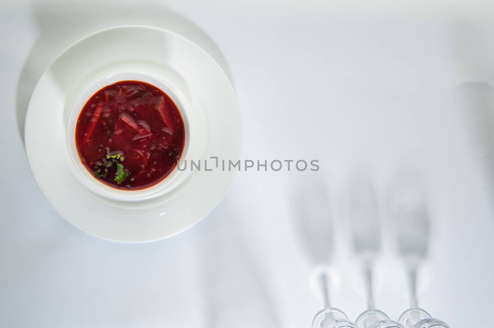 soup in a plate on a white surface with a shadow from the wine glasses
