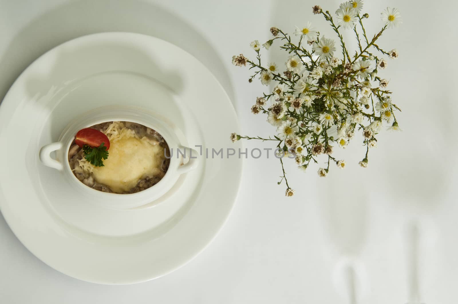 mushroom soup and chamomile flowers on a white surface with a shadow from the wine glasses