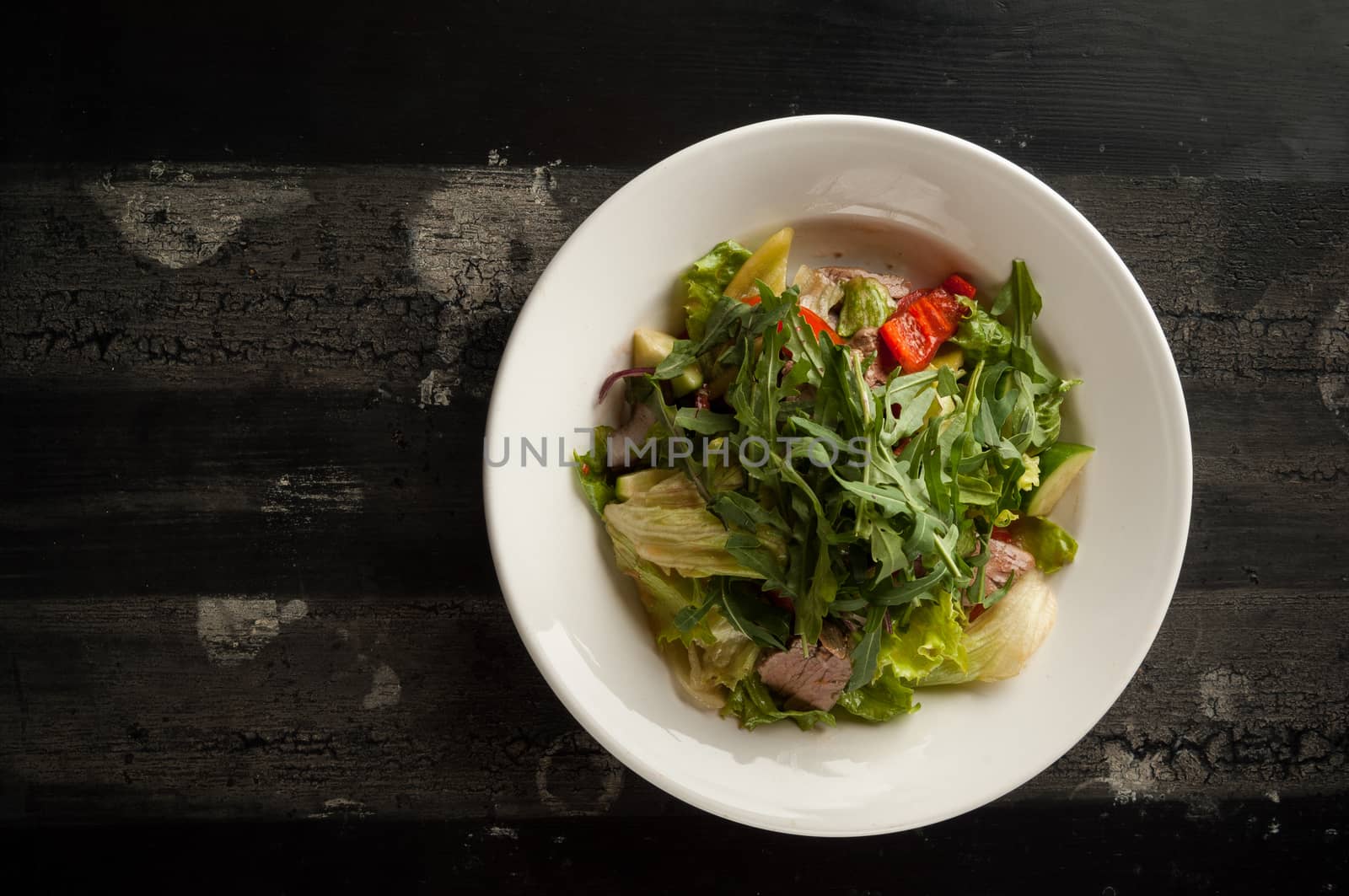 meat salad in a white plate on a wooden old surface