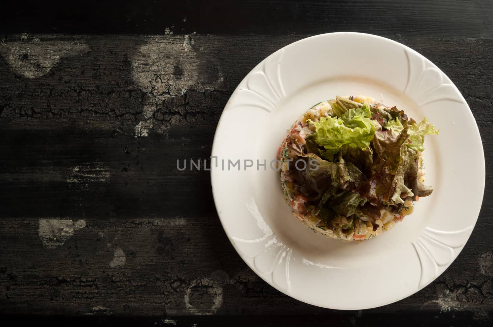 salad olivier in a white plate on a wooden old surface. Olivier salad with greens in a round plate on a wooden old board